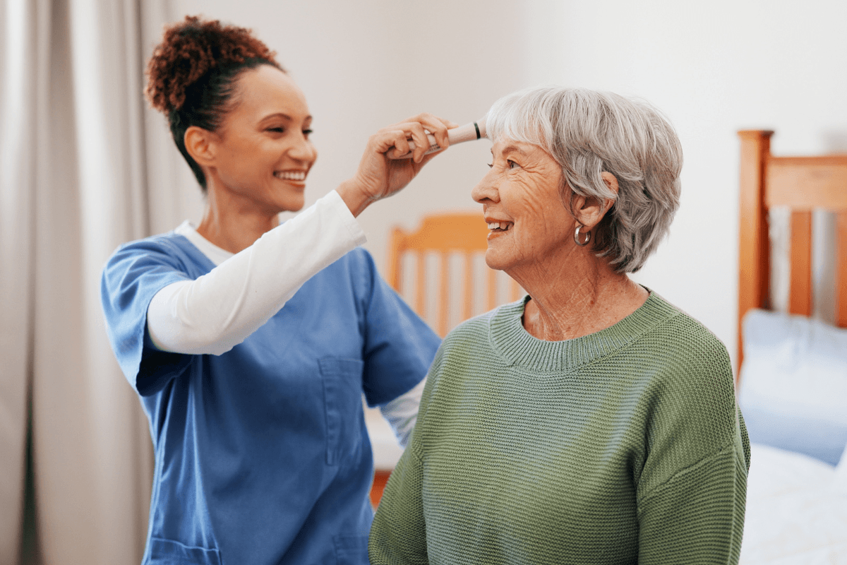 Senior woman, nurse and brush for hair care in bedroom, happy and helping hand with grooming routine. Elderly person, caregiver and comb with smile, conversation or assisted living in retirement home